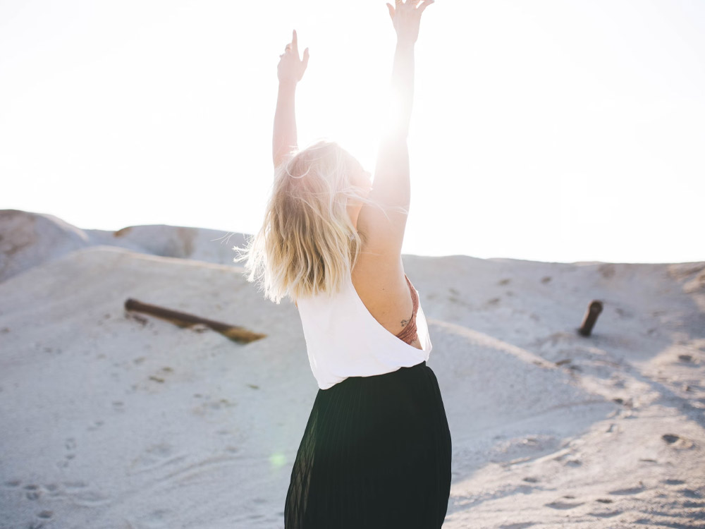 Showing a woman raising her arms to the sun. Hero image for Integrative Mental Health page, Recovery Without Walls.